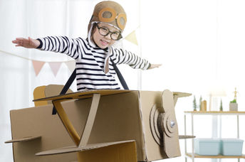 Creative little girl uses her imagination as she ‘flies’ in a cardboard box.