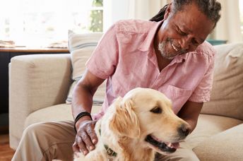 Senior man sitting on sofa at home with pet labrador dog.