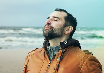 A man on the beach doing deep breathing exercises.