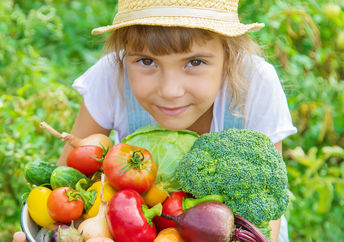 A young girl in a field holds a basket filled with freshly-picked vegetables.