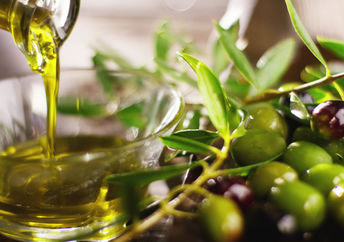 Pouring cold pressed olive oil into a bowl beside a branch of olives.