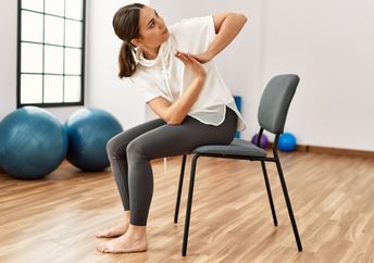 Woman performing chair yoga at a fitness center.