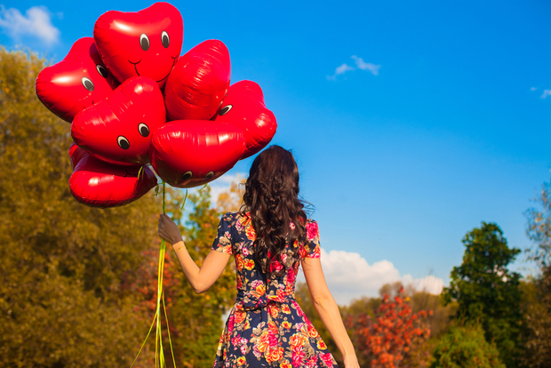 Woman wears floral dress and holds smiley balloons