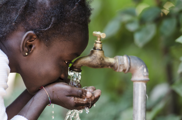 A young African girl drinking clean water from a tap