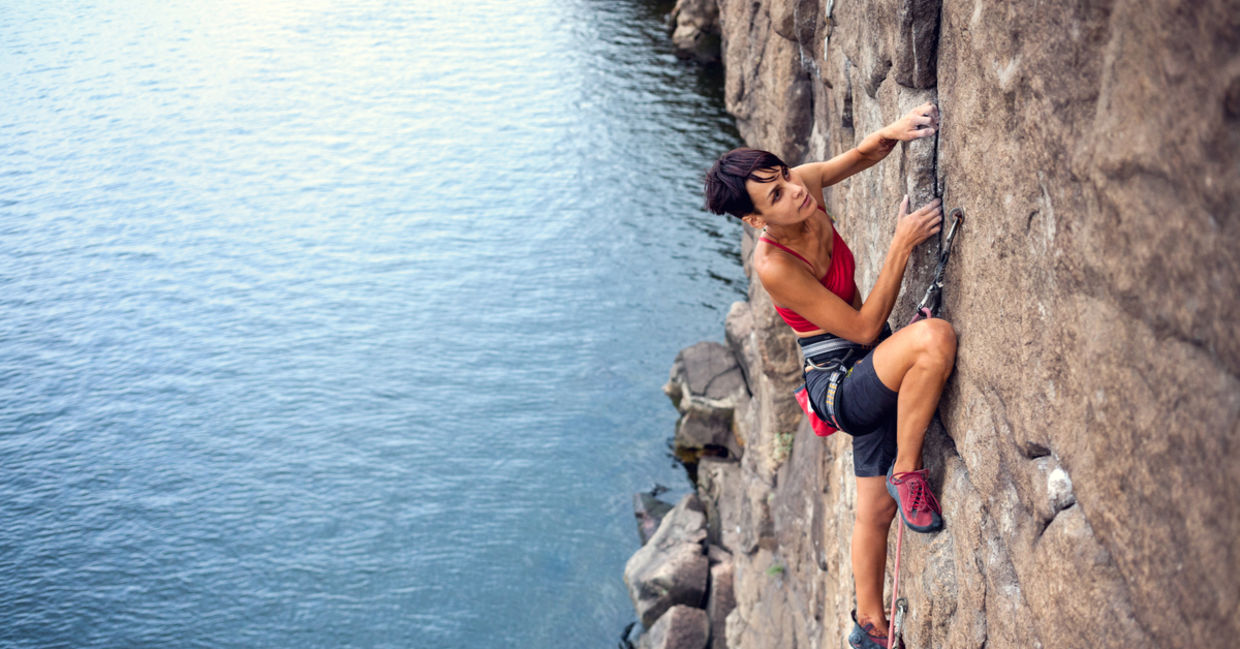 take a risk - Female climber dangles from the edge of a challenging cliff