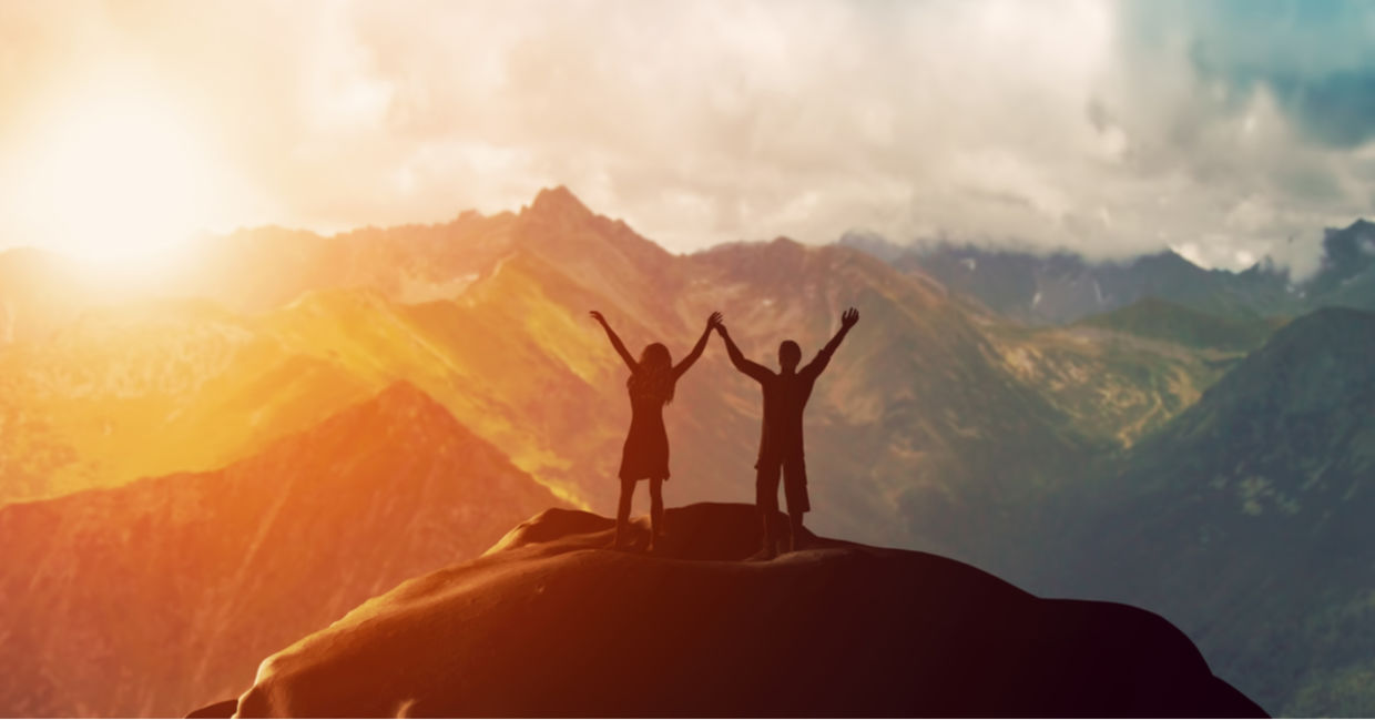 Couple standing on mountain with arms raised