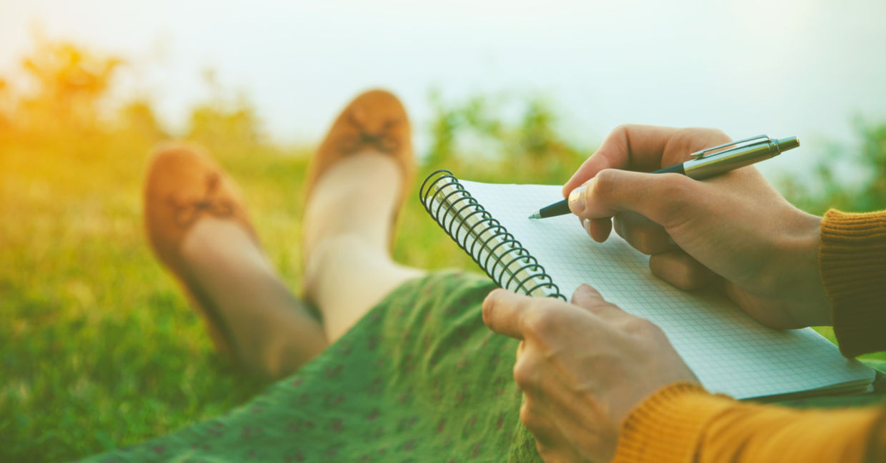 A woman writes in a journal while sitting in nature.
