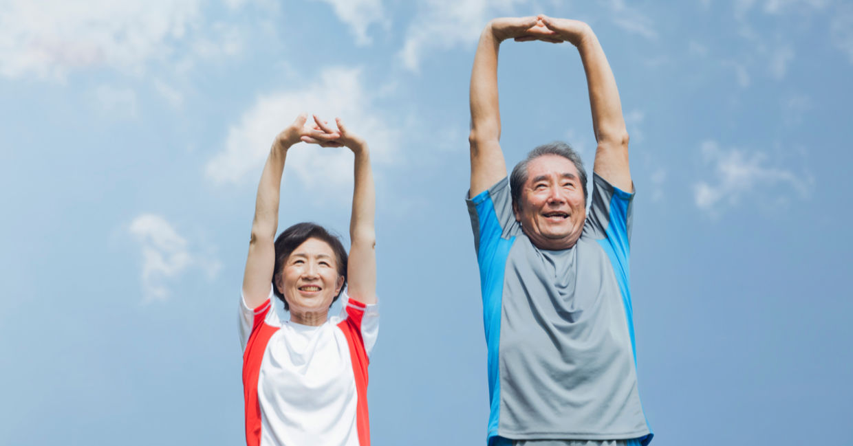 Older Japanese couple stretching under a blue sky.