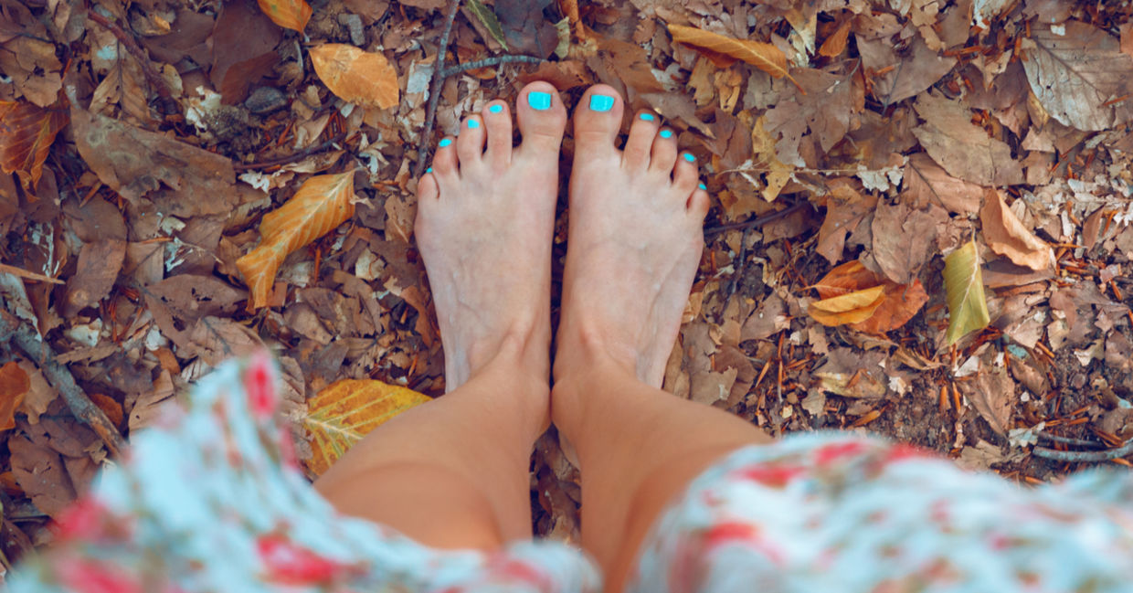 A woman stands barefoot on autumn leaves.