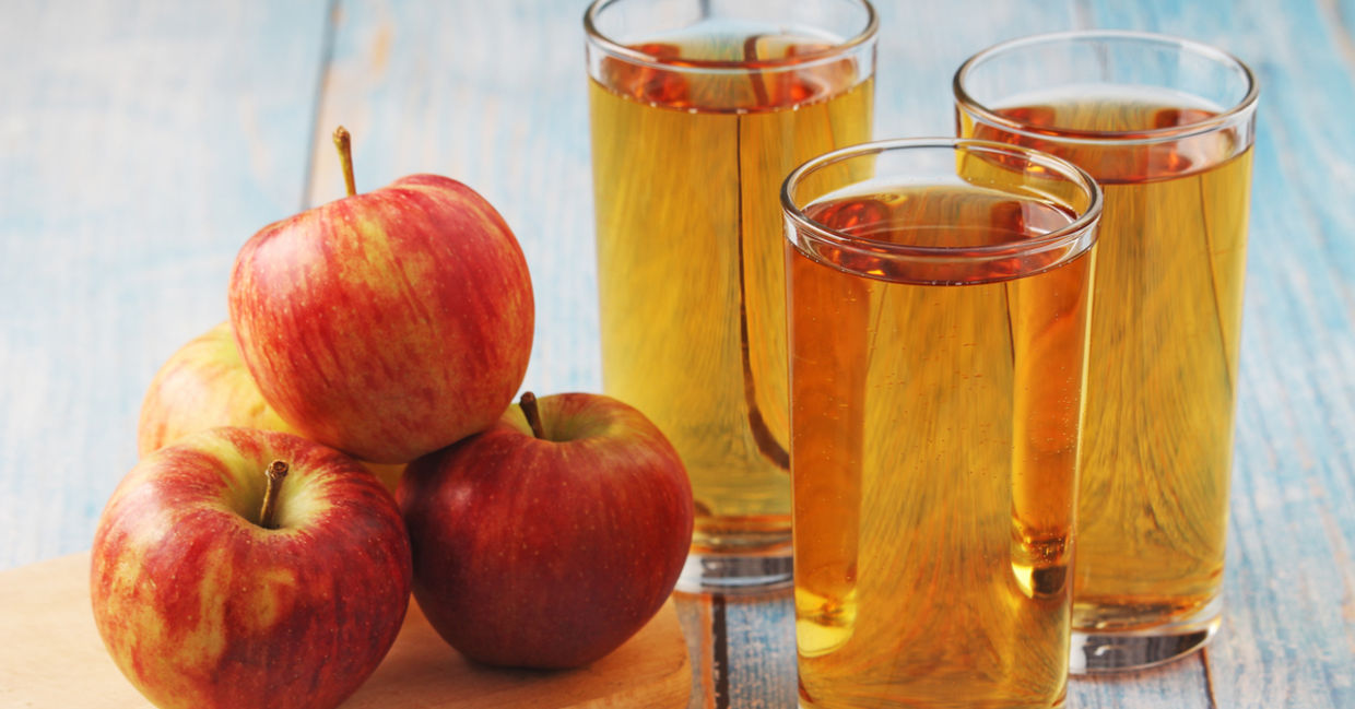 Glasses of homemade apple juice placed beside apples.