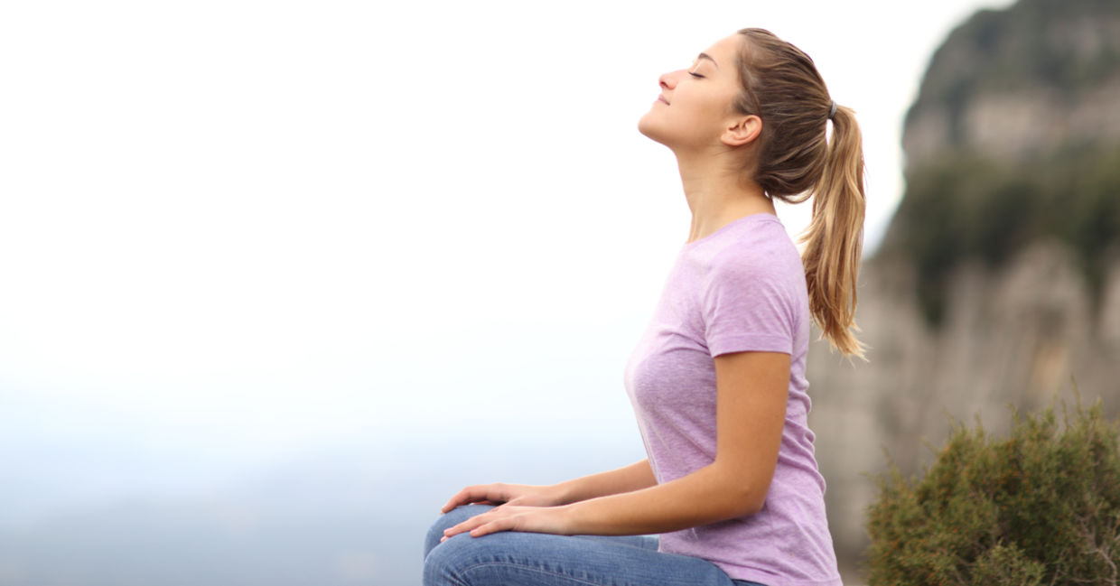 A woman focuses on her breath as she practices a mindful meditation outside.