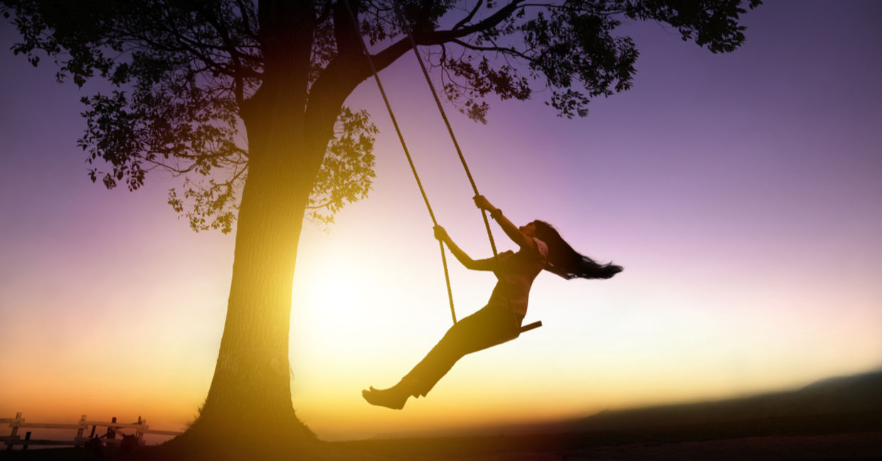Silhouette of joyful woman on a swing with sunset background