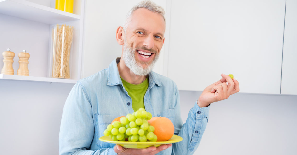 A middle-aged man holds a plate of green grapes.