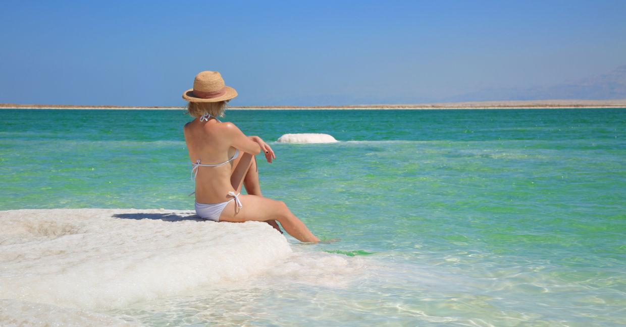 A woman sits on a salt-packed shore of the Dead Sea in Israel.