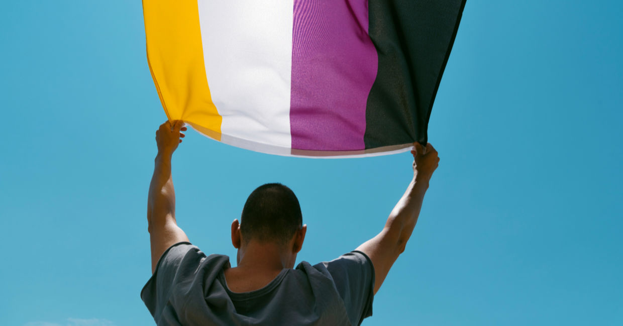Holding up a nonbinary flag ag a Gay Pride parade.