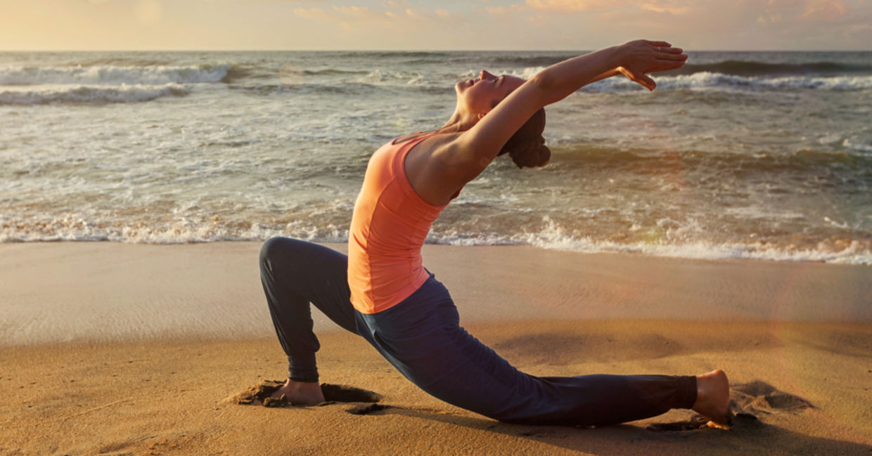 A woman practices the crescent lunge yoga pose on the beach.
