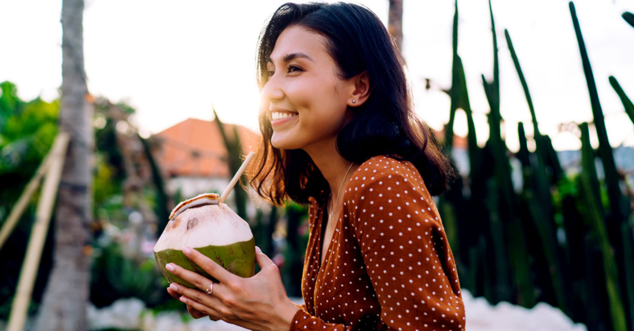 Woman enjoying a coconut water drink through a straw on a sunny evening.