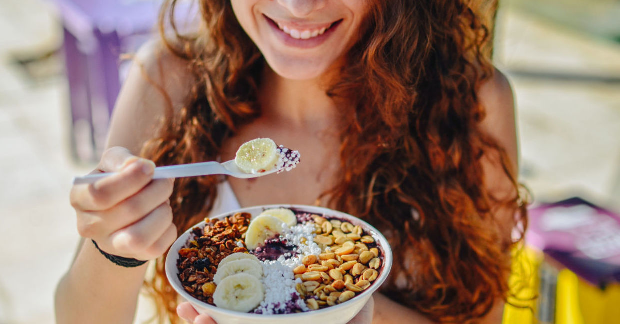 A woman eats a bowl of oats with bananas and nuts, all rich in tryptophan.