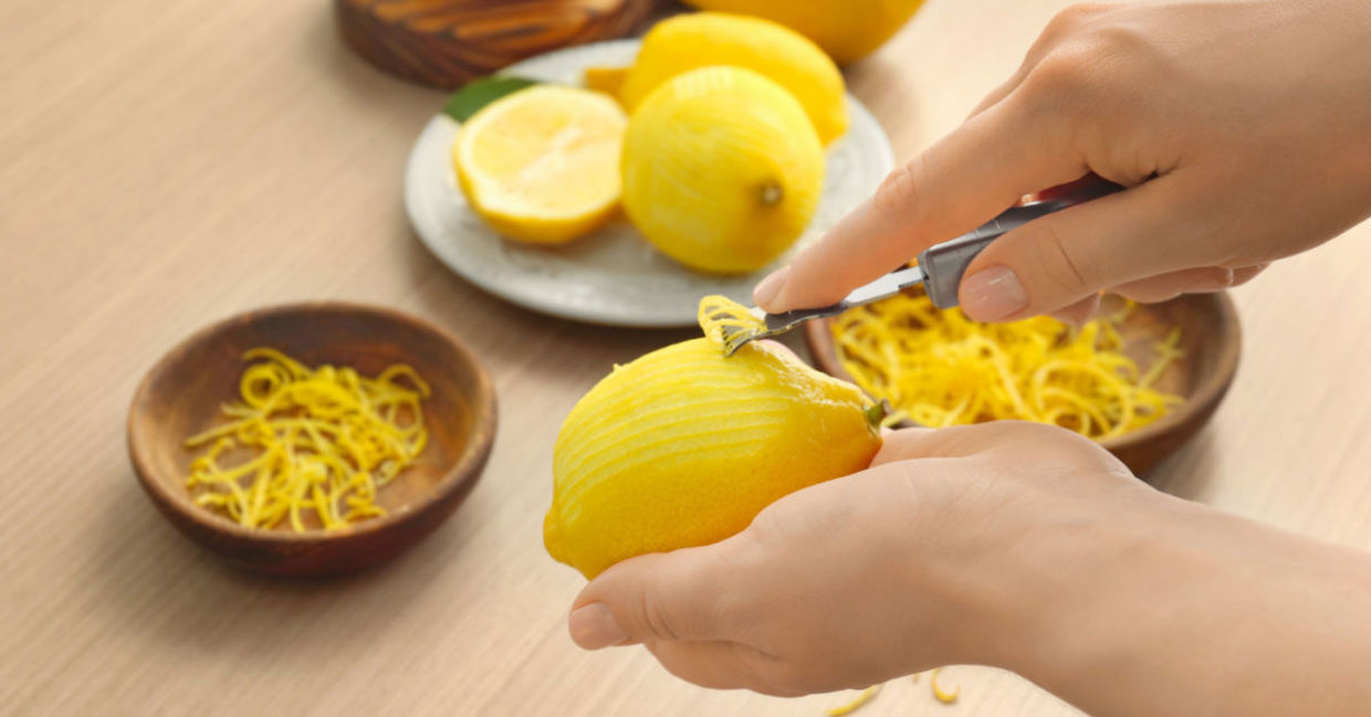 A woman peels a lemon with a zester.