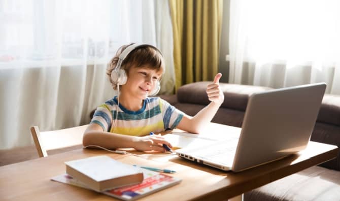 A boy wearing headphones gives a thumbs-up while using his laptop.