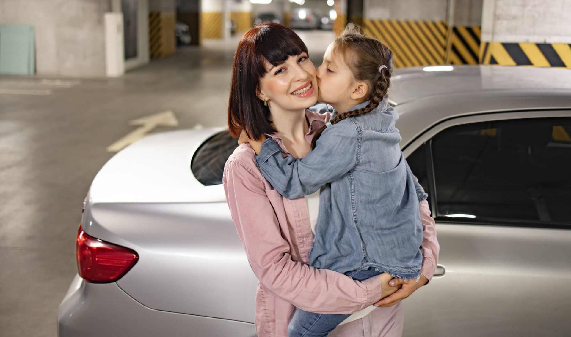 A woman carries a girl in an underground parking lot.