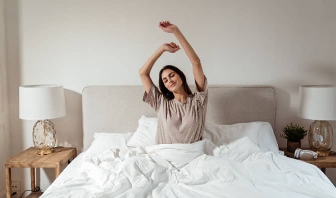 A smiling young woman stretching in bed.