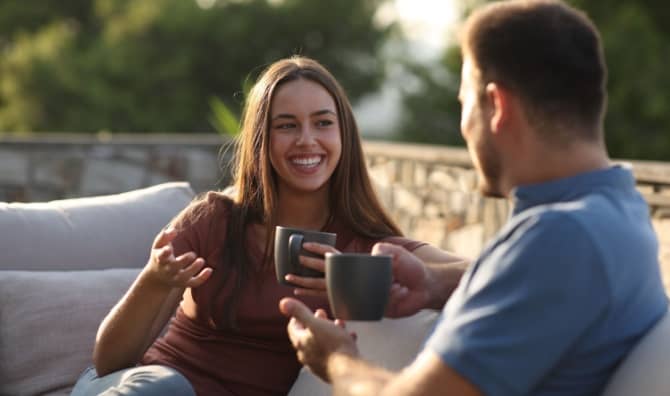 A happy woman talking with a friend drinking coffee on a terrace.