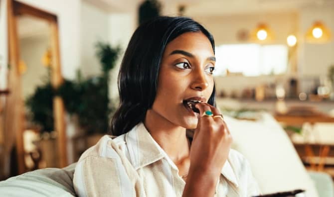 A woman eats a piece of chocolate in a living room.