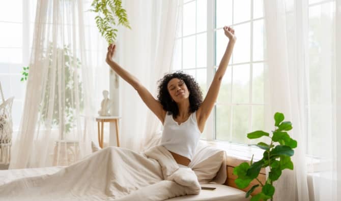 A happy woman stretching in bed after waking up.