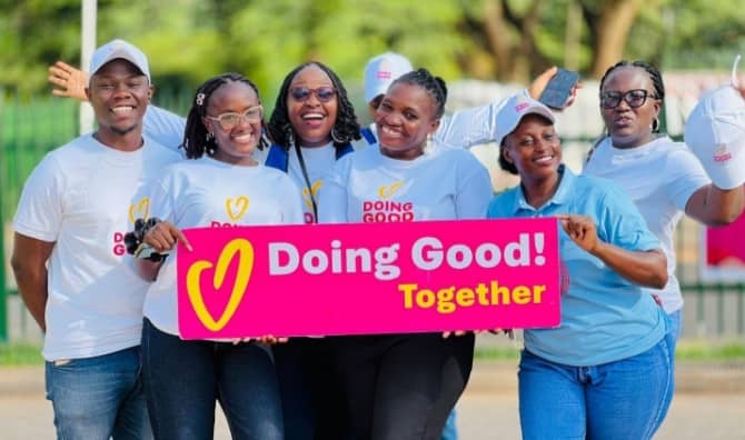 Volunteers in Uganda smile while holding a bright pink "Doing Good! Together" sign.