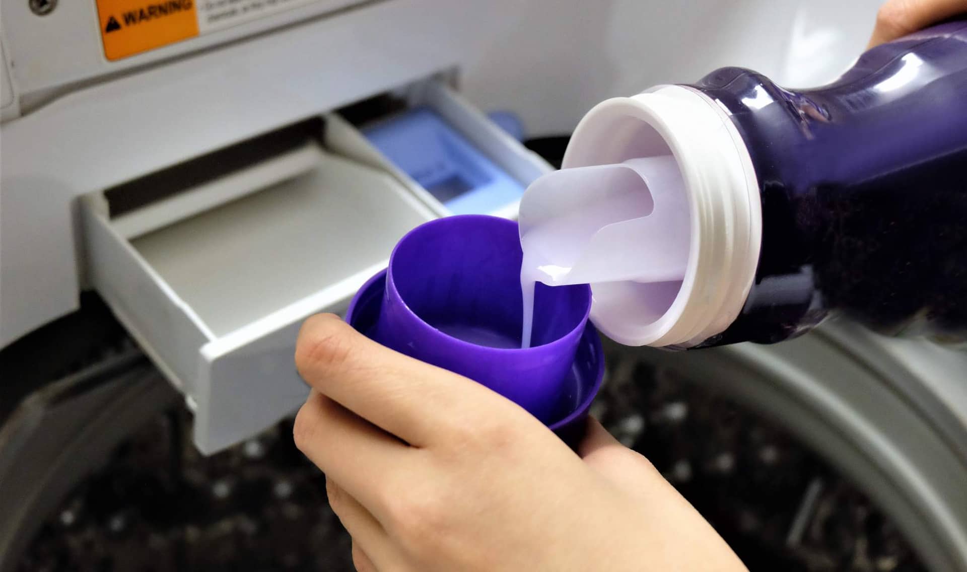 Putting laundry detergent into a washing machine.