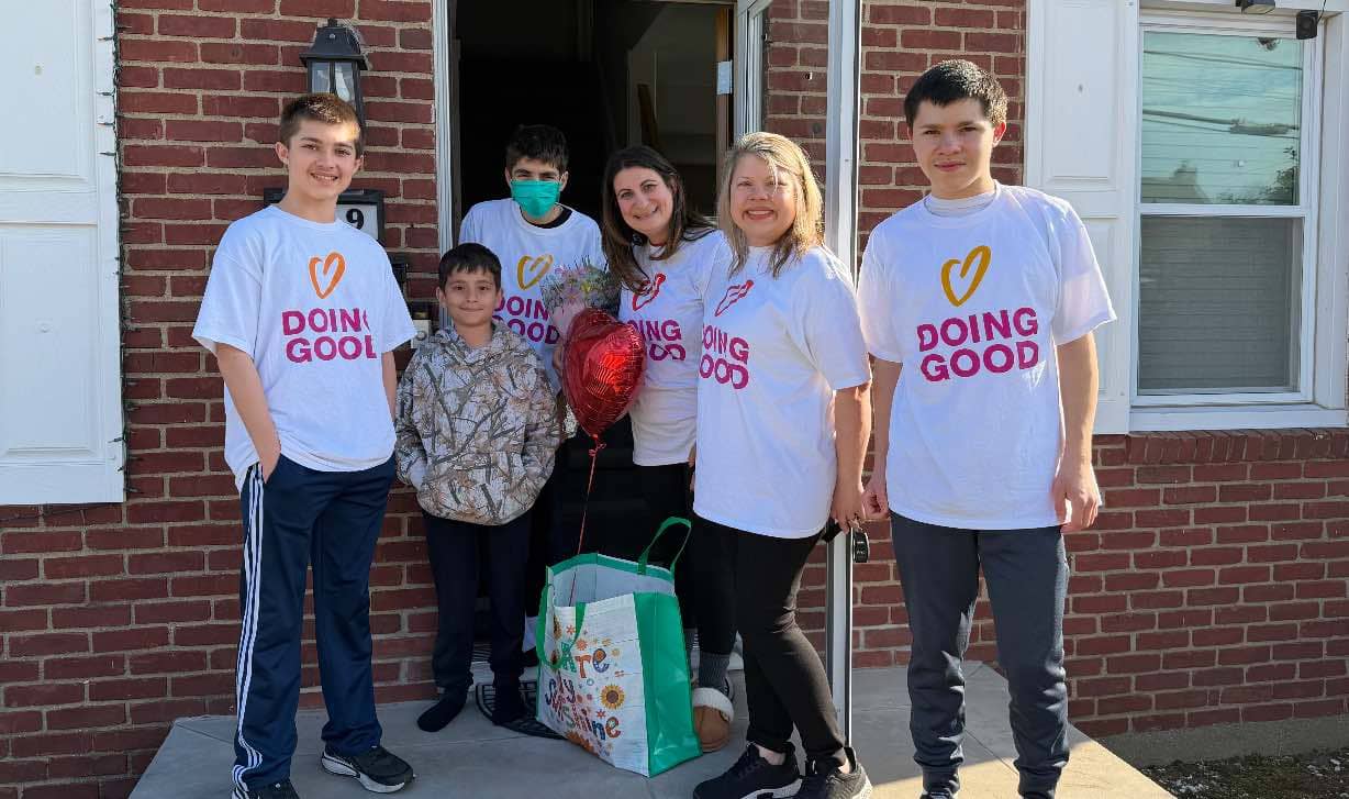 A group of people wearing Doing Good T-shirts standing outside a home.
