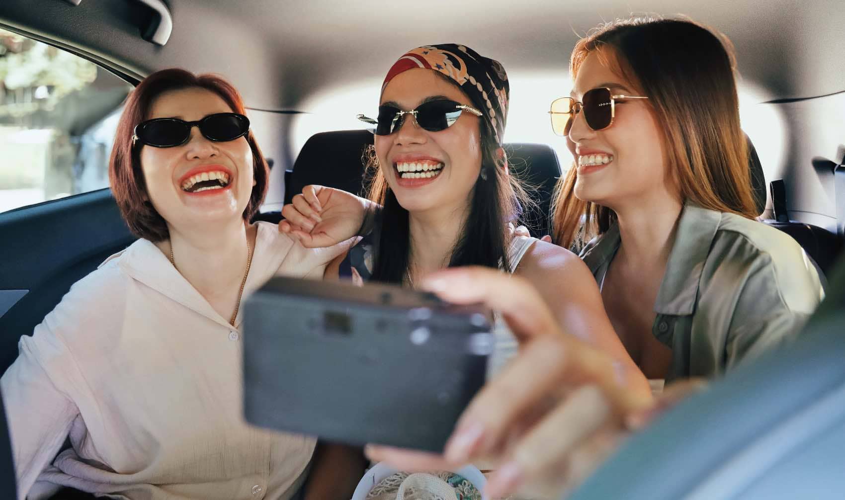 Three women wear sunglasses and take a selfie.