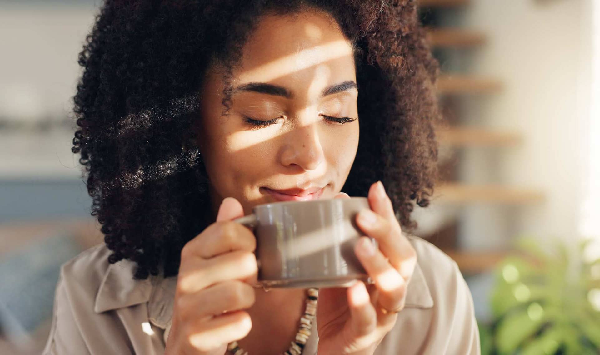 A smiling woman holding a cup of coffee by a window.