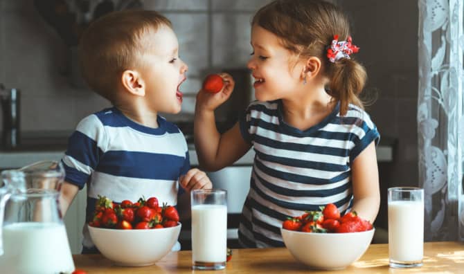 Two children eating strawberries and drinking milk.
