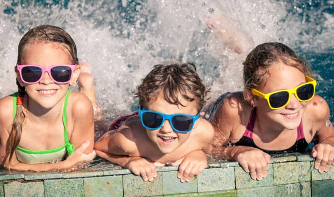 Three children wearing sunglasses at swimming pool edge.