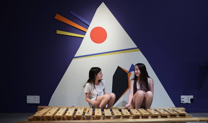 Two girls play with an instrument.