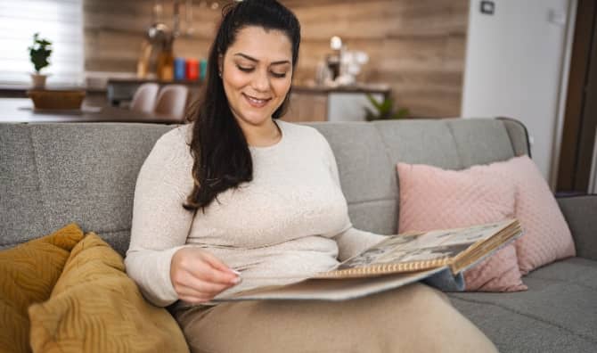 A woman looking at a photo album while sitting on a couch.