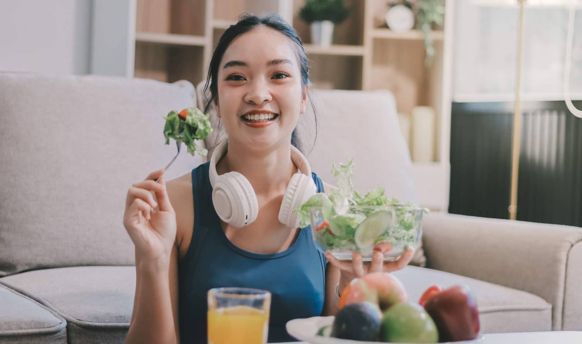 A woman in activewear sits and eats a fresh vegetable salad.