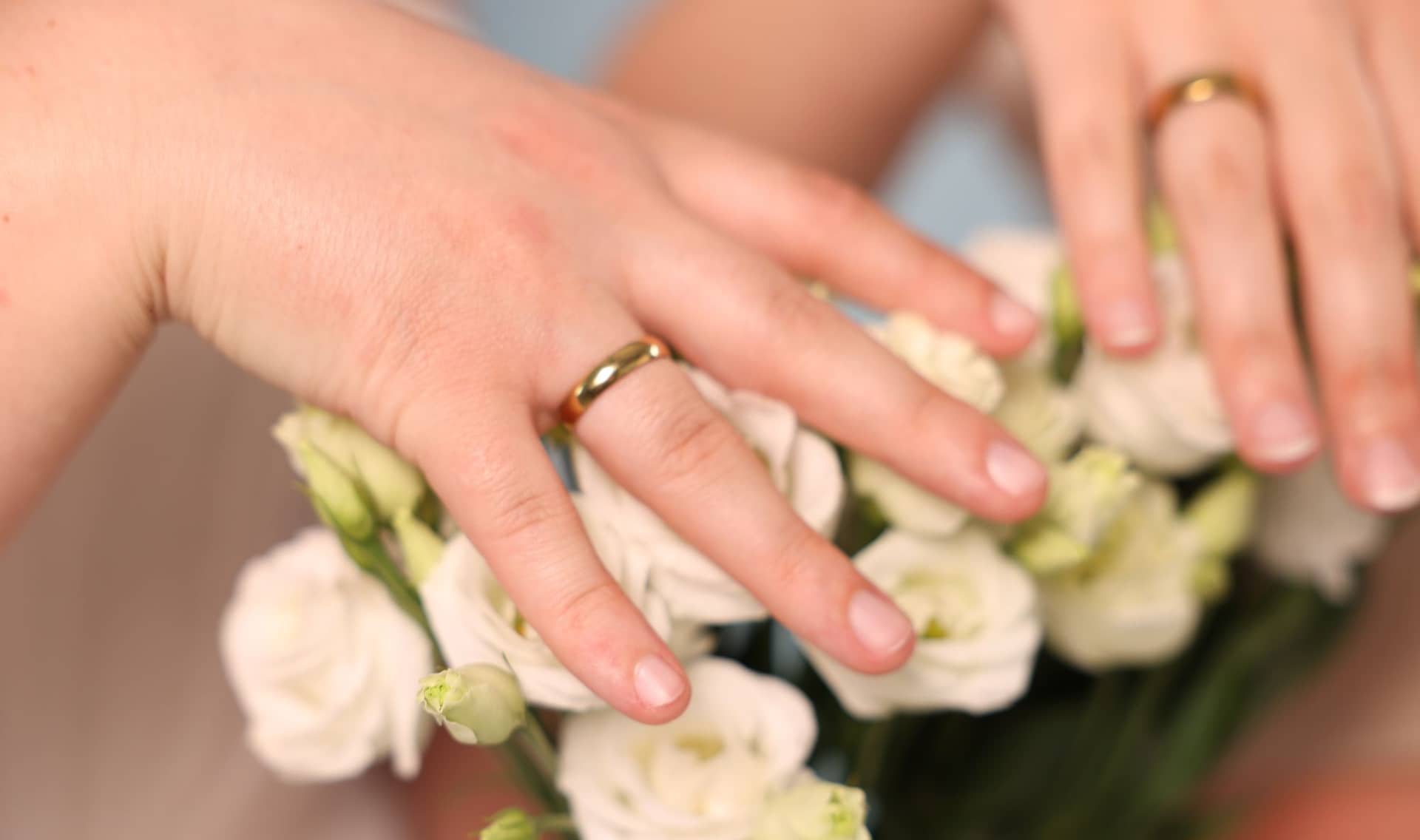 Two brides with beautiful flowers show their wedding rings.