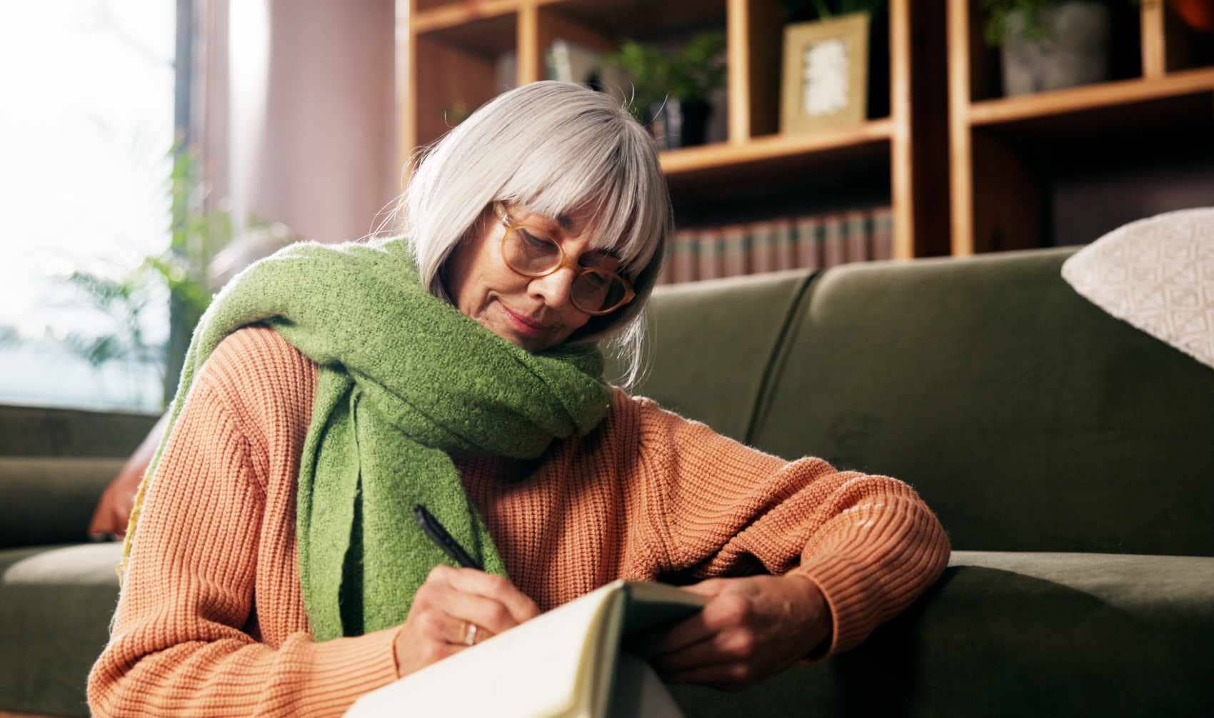A woman writes in a book on a living room floor.
