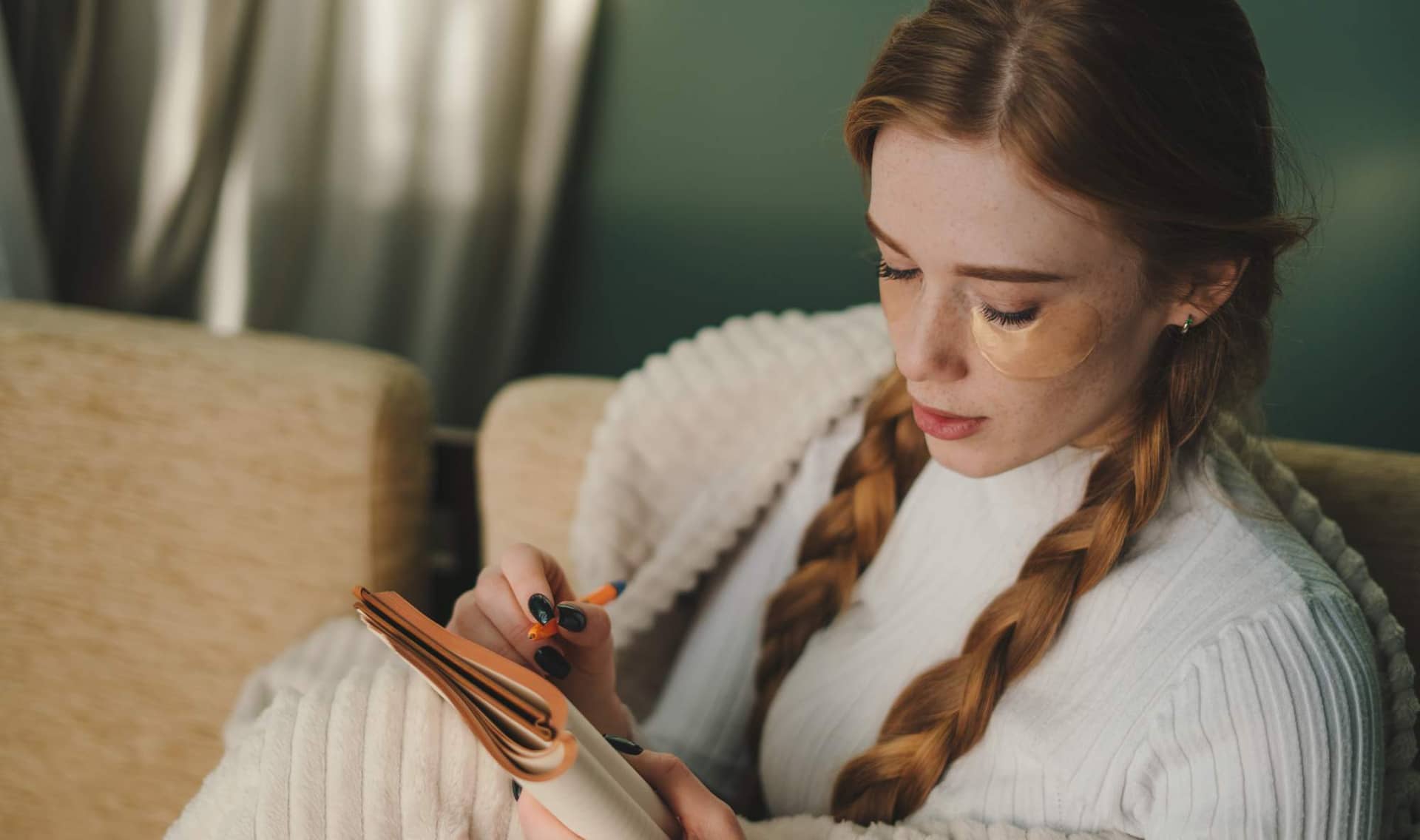A woman writes down memories in a notebook while sitting on a sofa.