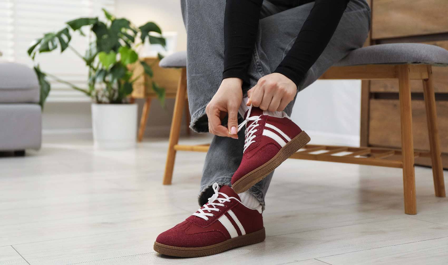 A woman ties her sneakers while sitting on a bench at home.