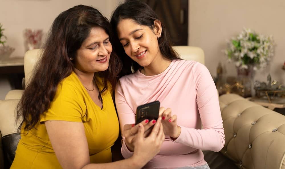 A cheerful Indian daughter teaching her mother about smartphones.