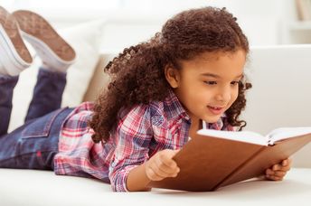 Young girl with curly hair reading a book on the floor