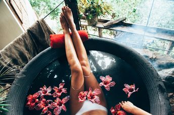 Woman relaxing in round outdoor bath with tropical flowers. Organic skin care in kawa hot bath in luxury spa resort.