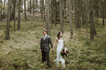 A couple in wedding dress and suit stand in the forest.