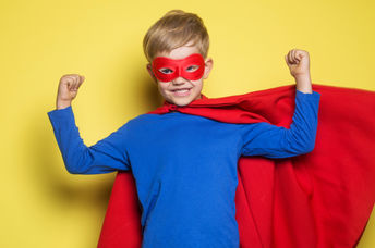 A young boy wearing a superhero mask and cape flexes his muscles and feels strong.