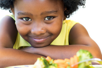 A young girl with a plate of healthy food smiles.