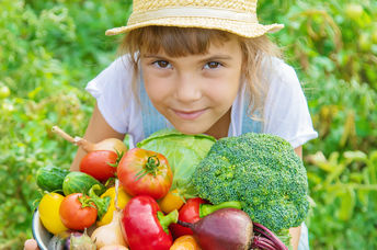 A young girl in a field holds a basket filled with freshly-picked vegetables.